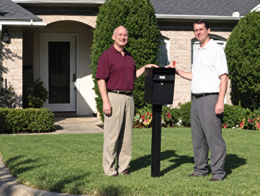 Founders Don and Steve beside a locking mailbox on a post in a front lawn