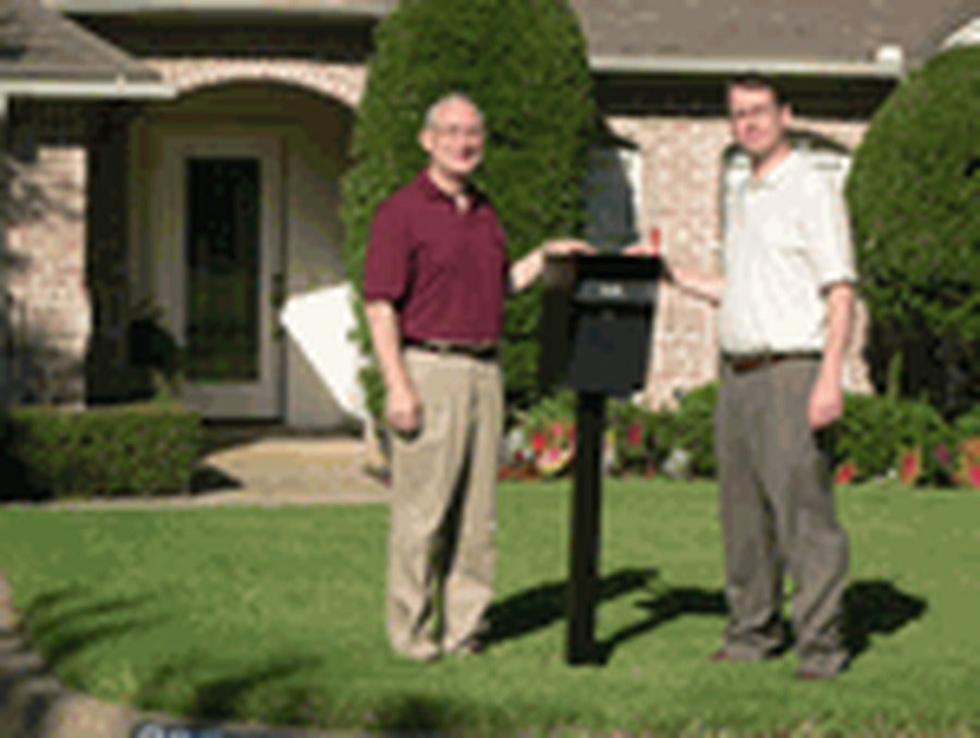 Founders Don and Steve beside a locking mailbox on a post in a front lawn